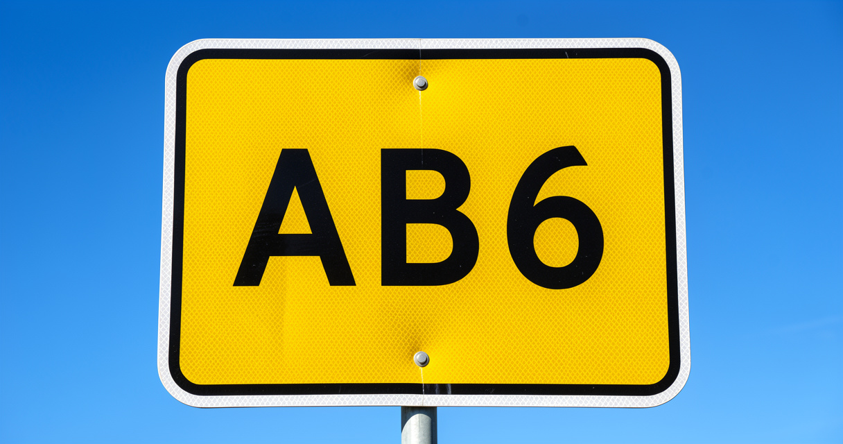Gros plan sur un panneau de route prioritaire AB6 avec bord blanc et surface jaune réfléchissante sous le soleil.